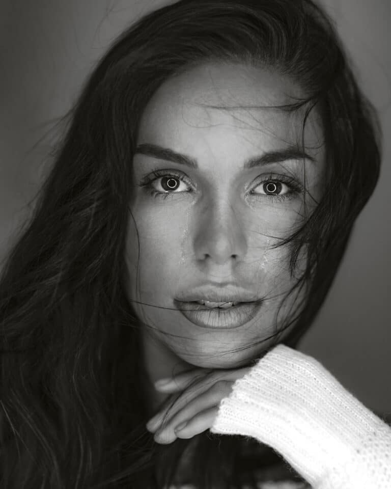 Black-and-white portrait in Mallorca – dark-haired model resting her face on a white knitted sleeve