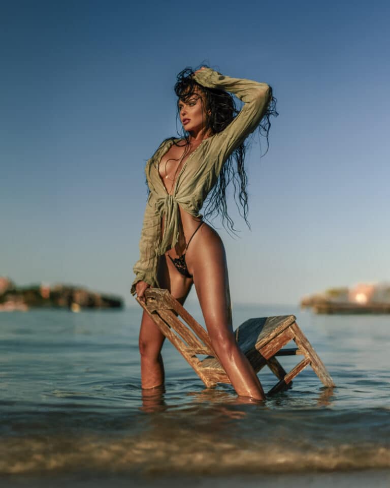 Fashion shoot in the sea at Cala Sa Nau, Mallorca – model in a sheer khaki blouse with a wooden chair in the water