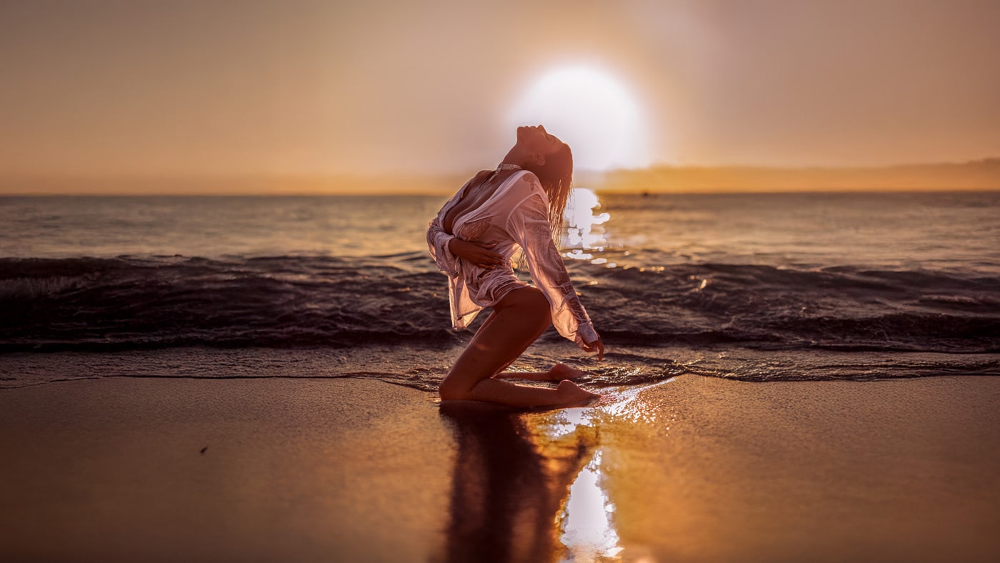 Sunset photoshoot on a beach in Mallorca – model in a white shirt kneeling in the shallow water